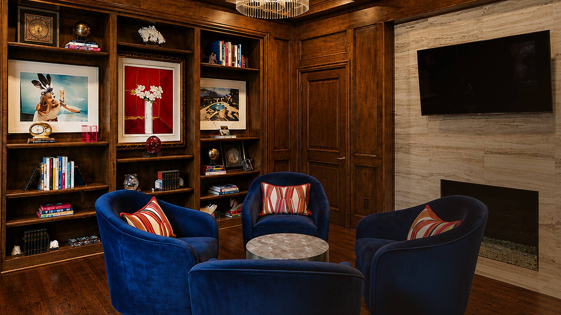 Wood-paneled library with navy velvet chairs, built-in shelving, and a fireplace