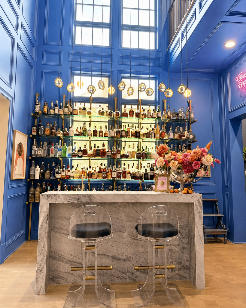 Two-story blue home bar with a marble waterfall counter and lit bottle shelving