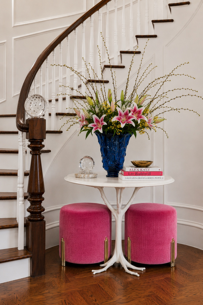 Curved staircase entry with a round table, lilies, and pink velvet ottomans