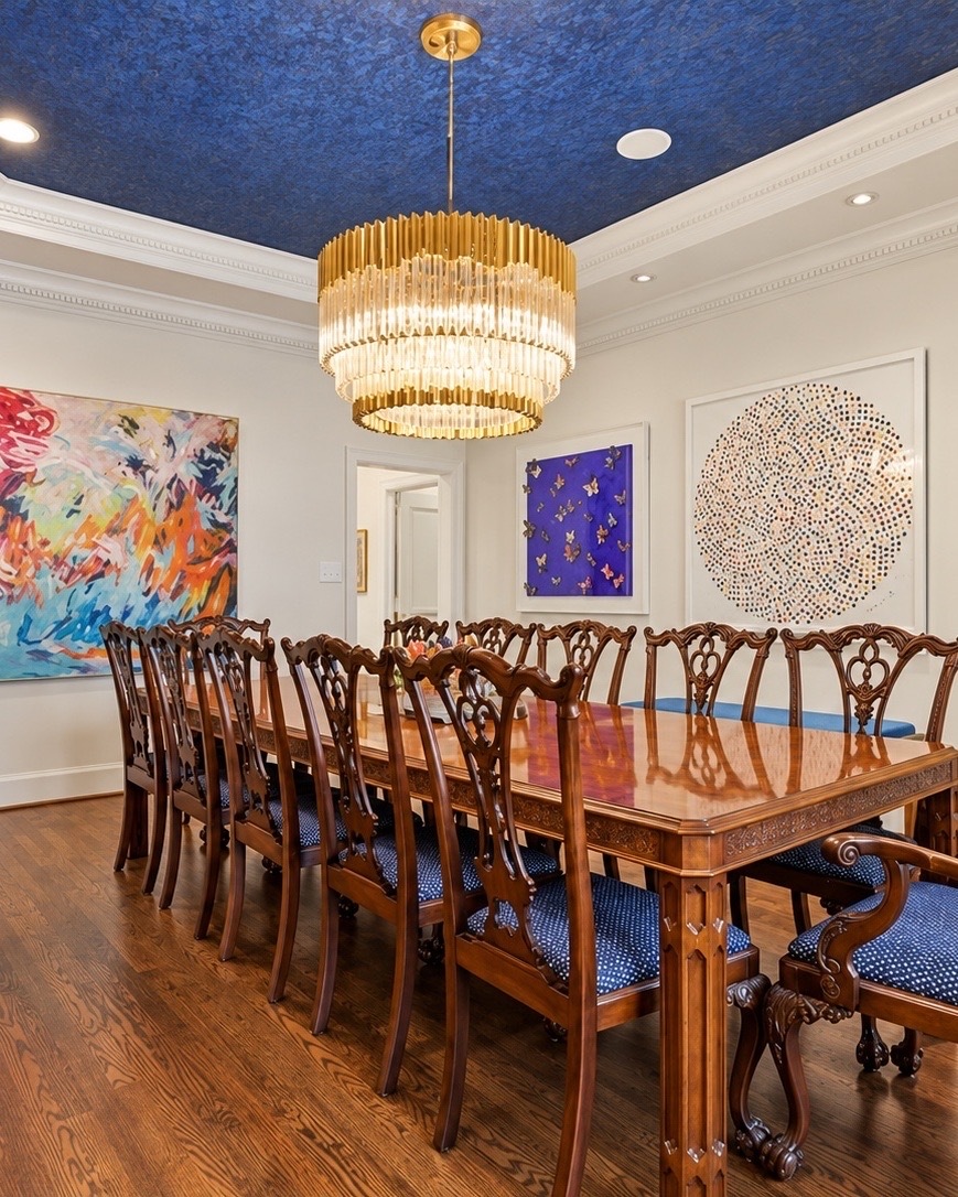 Dining room with a blue ceiling, gold chandelier, and colorful abstract art