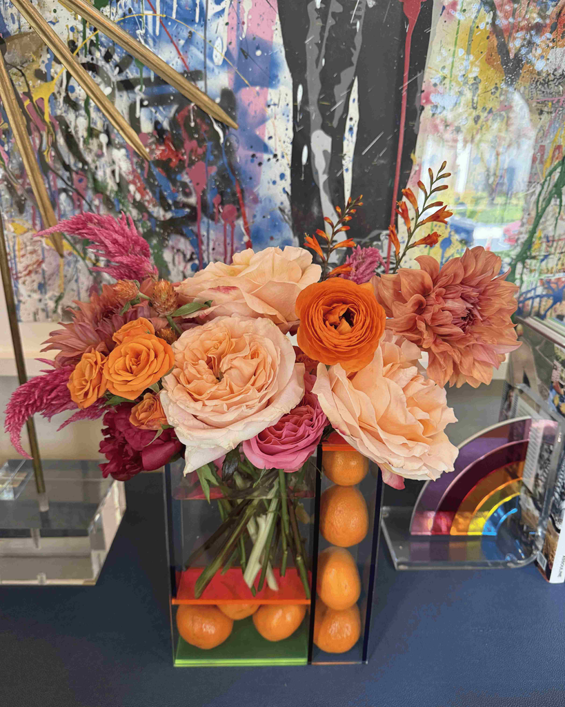 Colorful arrangement of peach roses and ranunculus in front of vibrant abstract artwork