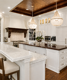 White kitchen with a marble island, crystal chandeliers, and a wood-paneled ceiling