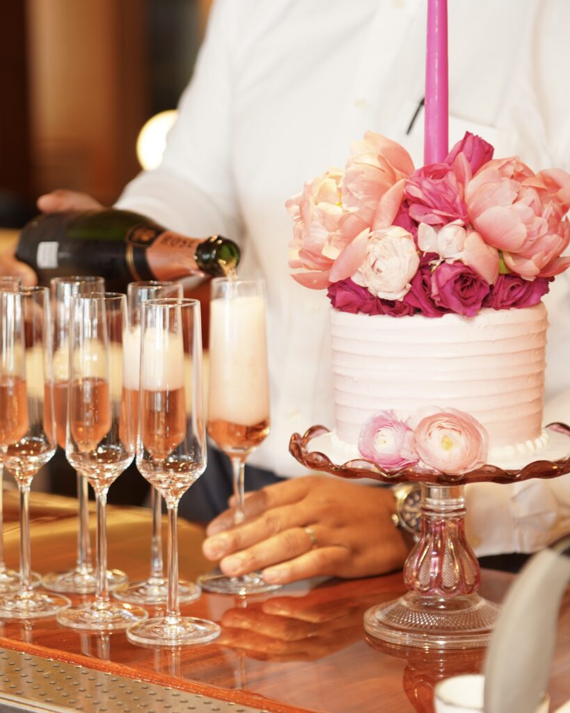 Champagne being poured beside a floral-topped celebration cake