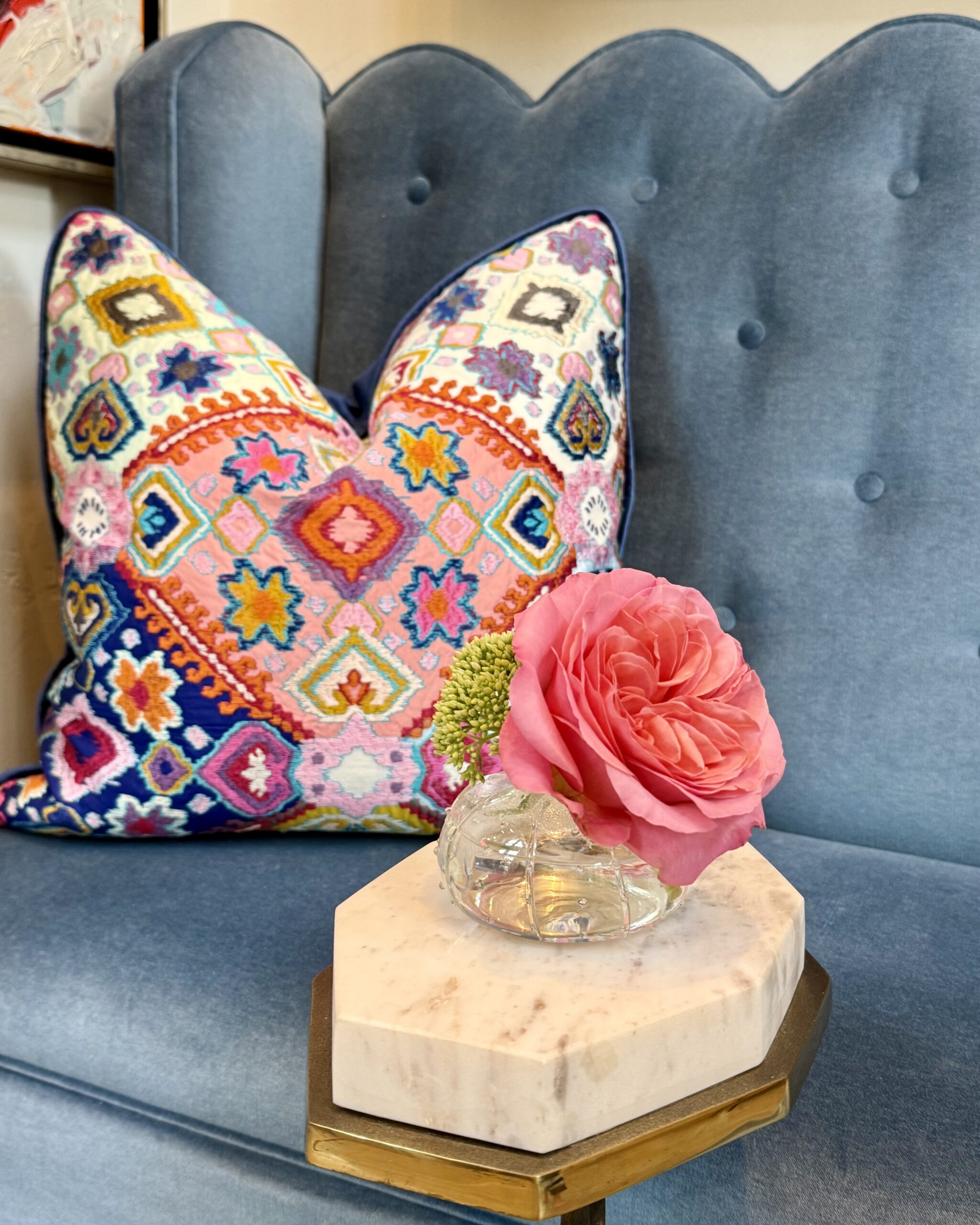 Embroidered pillow and a pink rose on a blue tufted velvet sofa