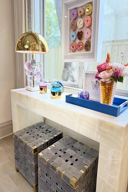 Onyx console table with a brass lamp, woven stools, and framed donut artwork