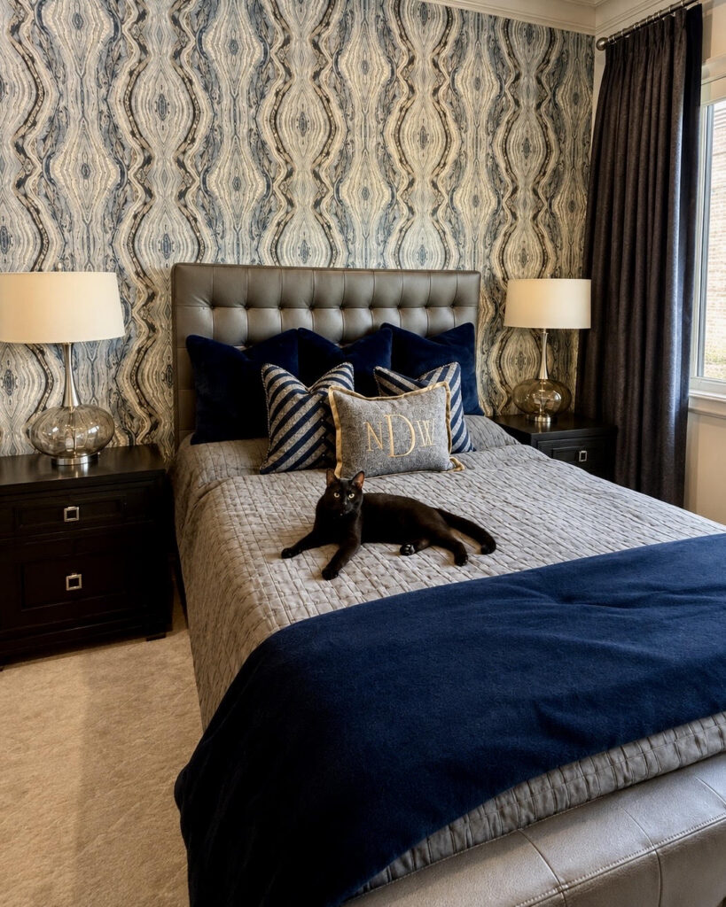 Bedroom with patterned wallpaper, a tufted headboard, and navy bedding