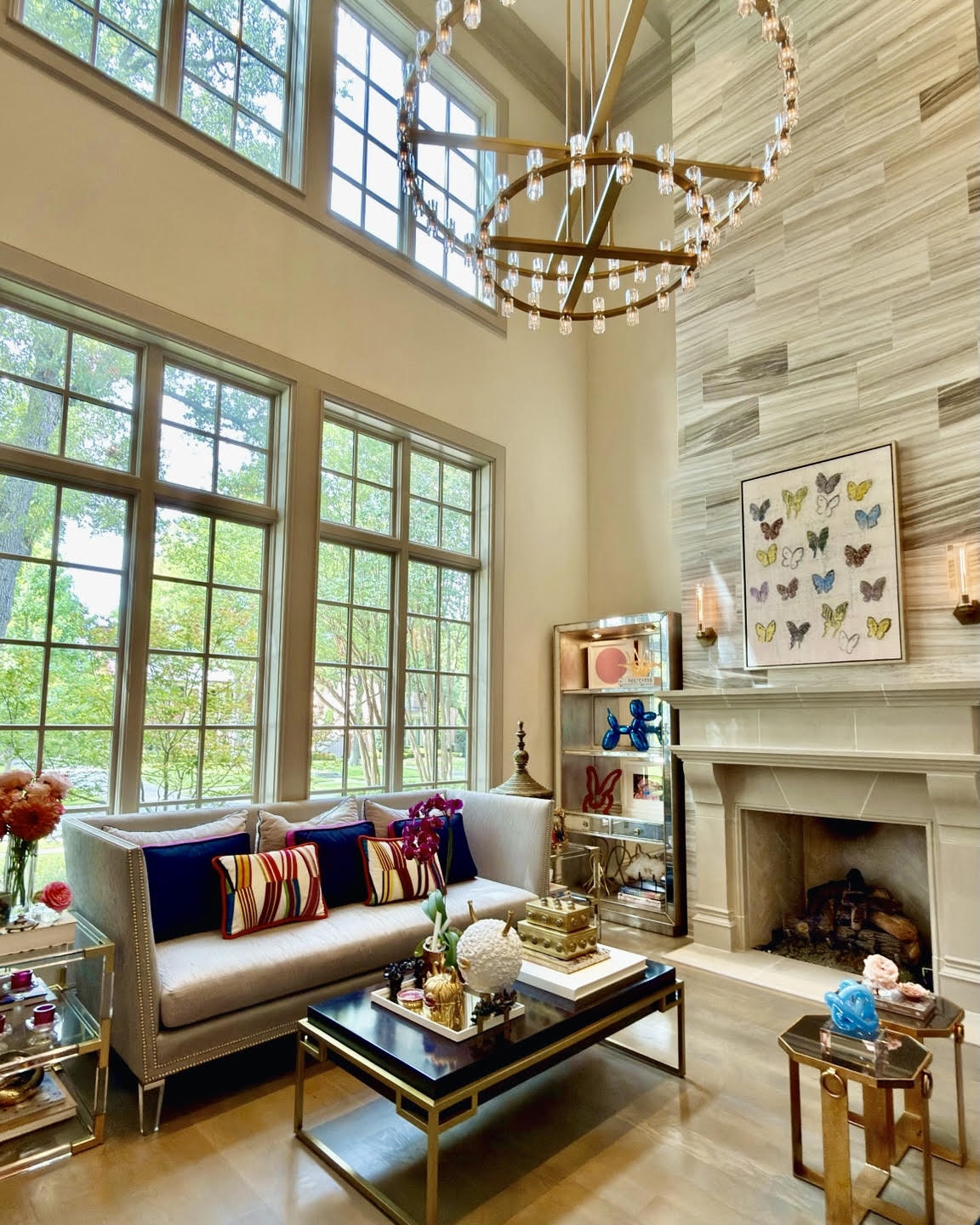 Two-story living room with a stone fireplace, ring chandelier, and butterfly artwork